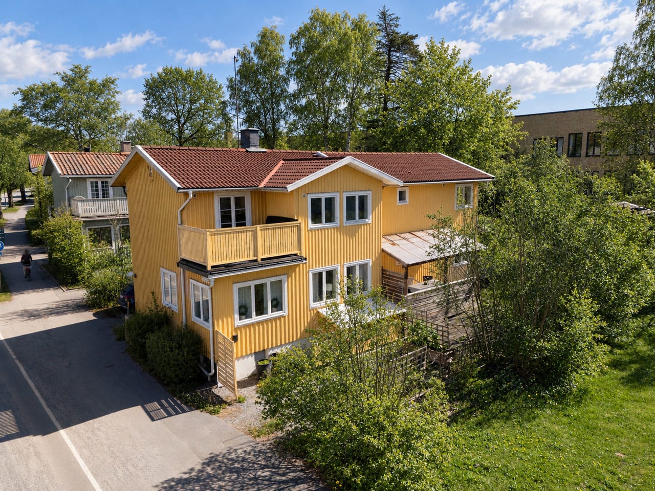 Gul villa i två plan med rött tegeltak och balkong, sedd snett uppifrån.