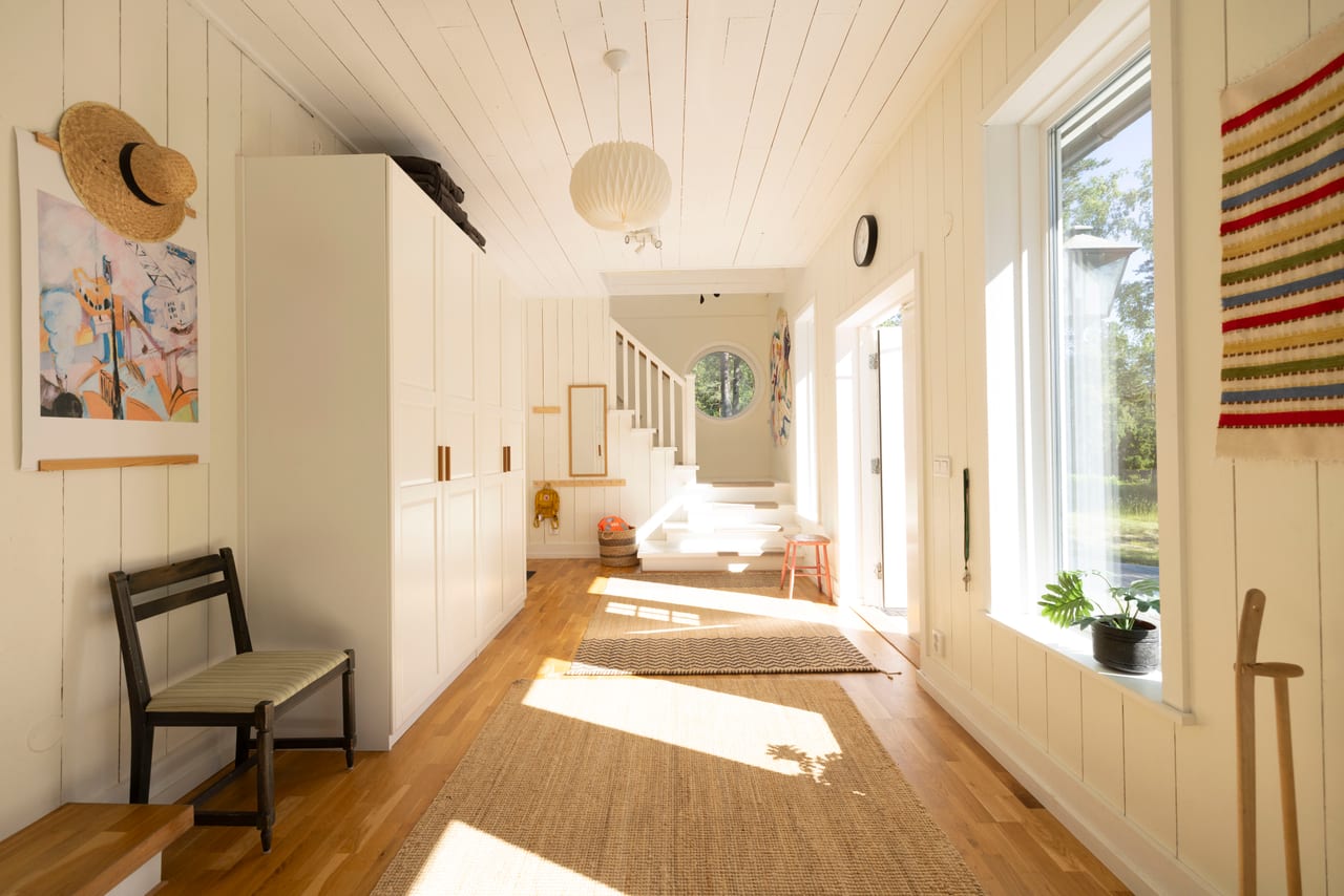 Ljus hall med jutemattor, trappa och öppen ytterdörr mot grönska.