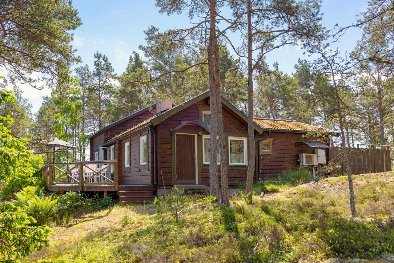 Rödbrunt timrat hus mellan tallar, sett framifrån.