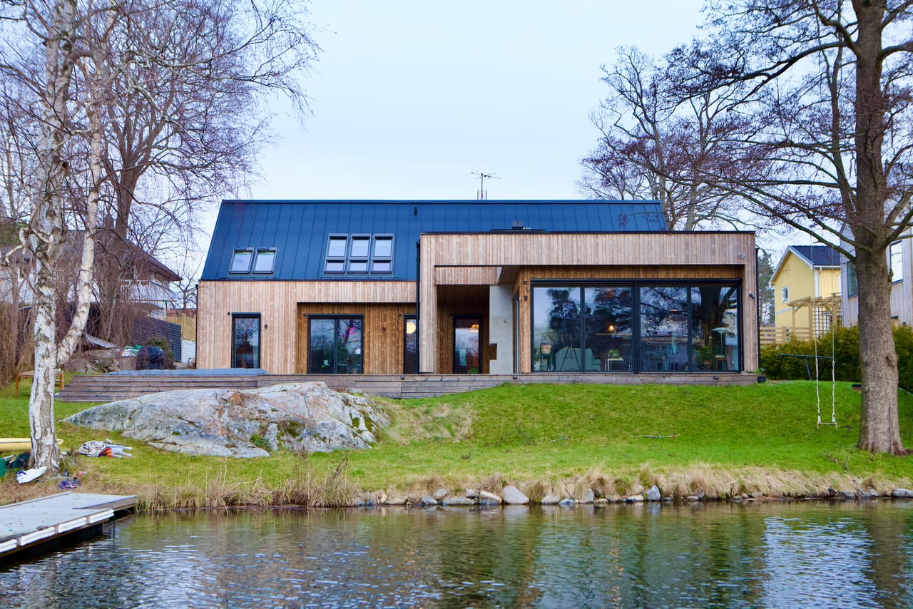 Modernt trähus med plåttak vid vattnet, med klippa och brygga.