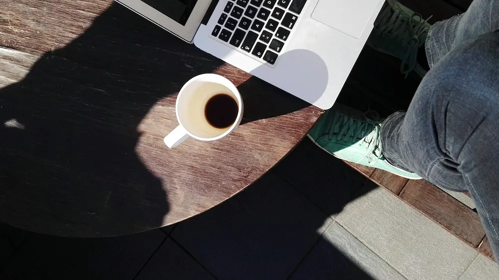 Bärbar dator och kaffekopp på ett bord, sett ovanifrån